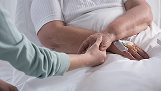 Someone holding hands with a person with a canula in a hospital bed.