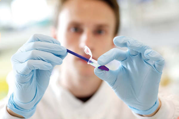 Researcher in a lab, holding a vial and pipette in gloved hands