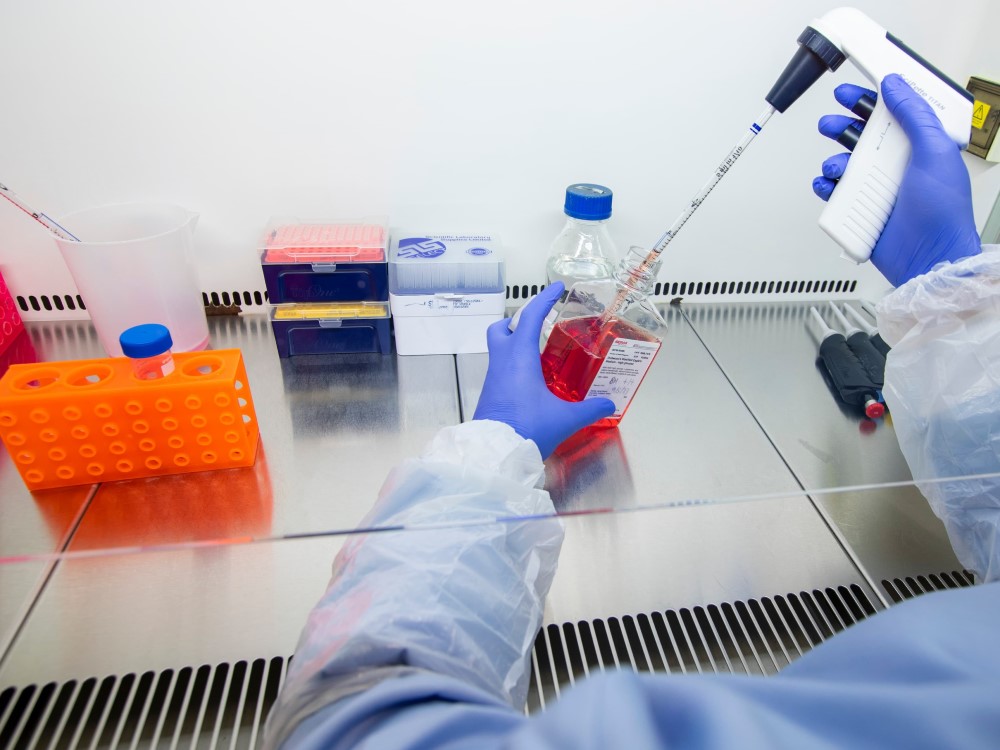 A researcher in a lab, extracting solution from a bottle using a large pipette