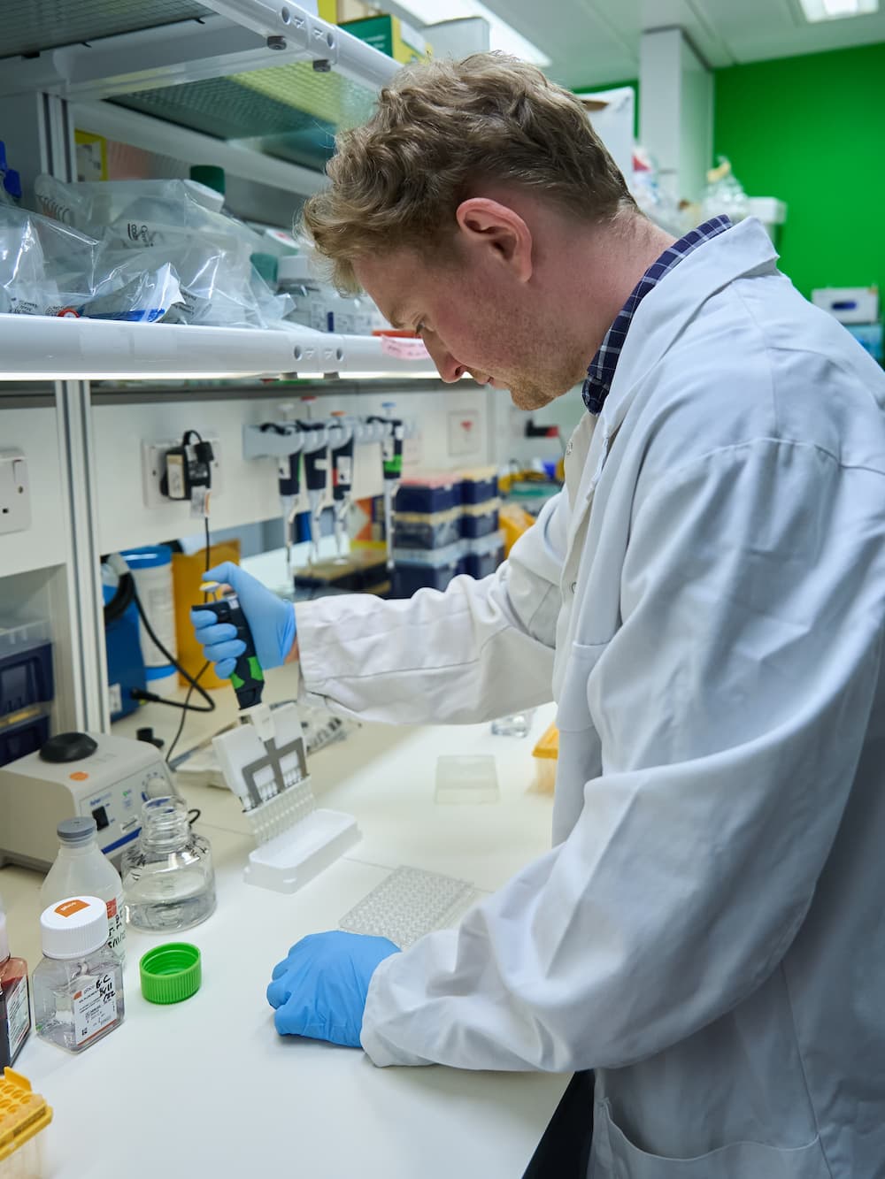 Dr Ben Clarke working in the lab. He is wearing a lab coat and blue gloves.