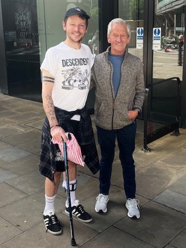 Jake, who is living with MND, standing next to his dad, Peter. They are outside a building.