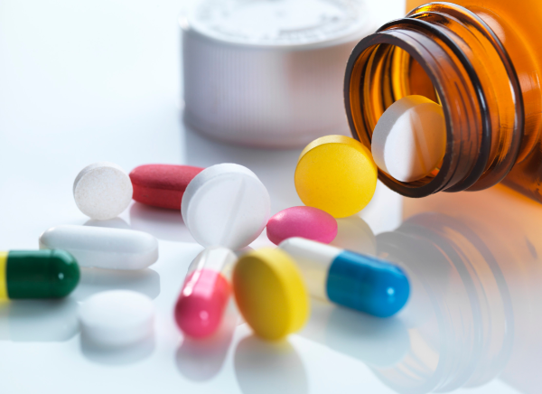 A photo of different coloured and shaped pills spilling from a bottle