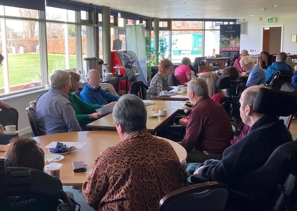 People living with and affected by MND sat around tables chatting at a support meeting