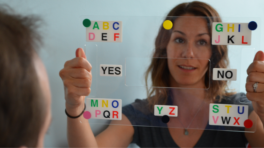 A woman holding an E-Tran frame, used to help people living with MND to communicate using an eye pointing technique.