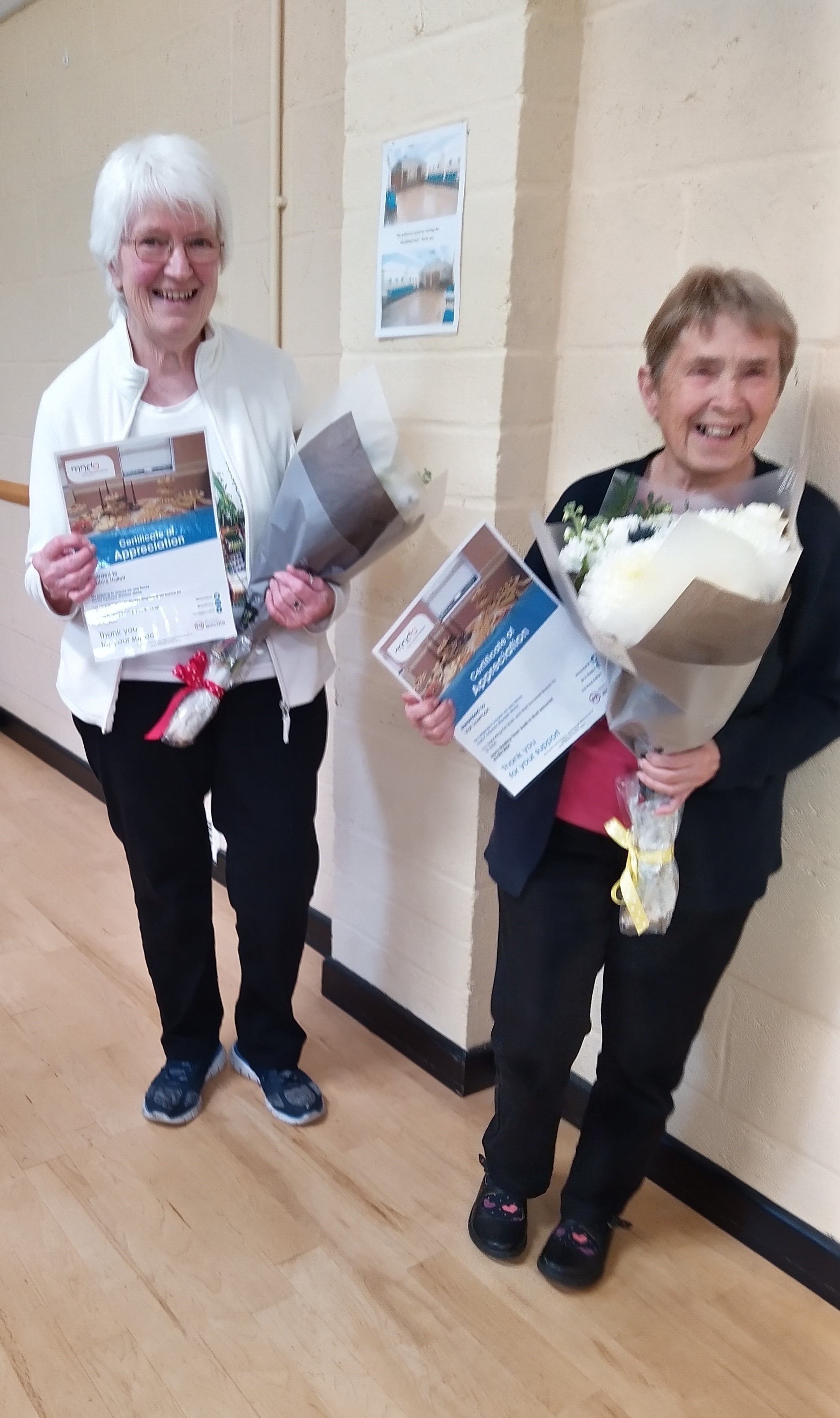 Daphne and Val smiling after receiving flowers and a certificate of appreciation