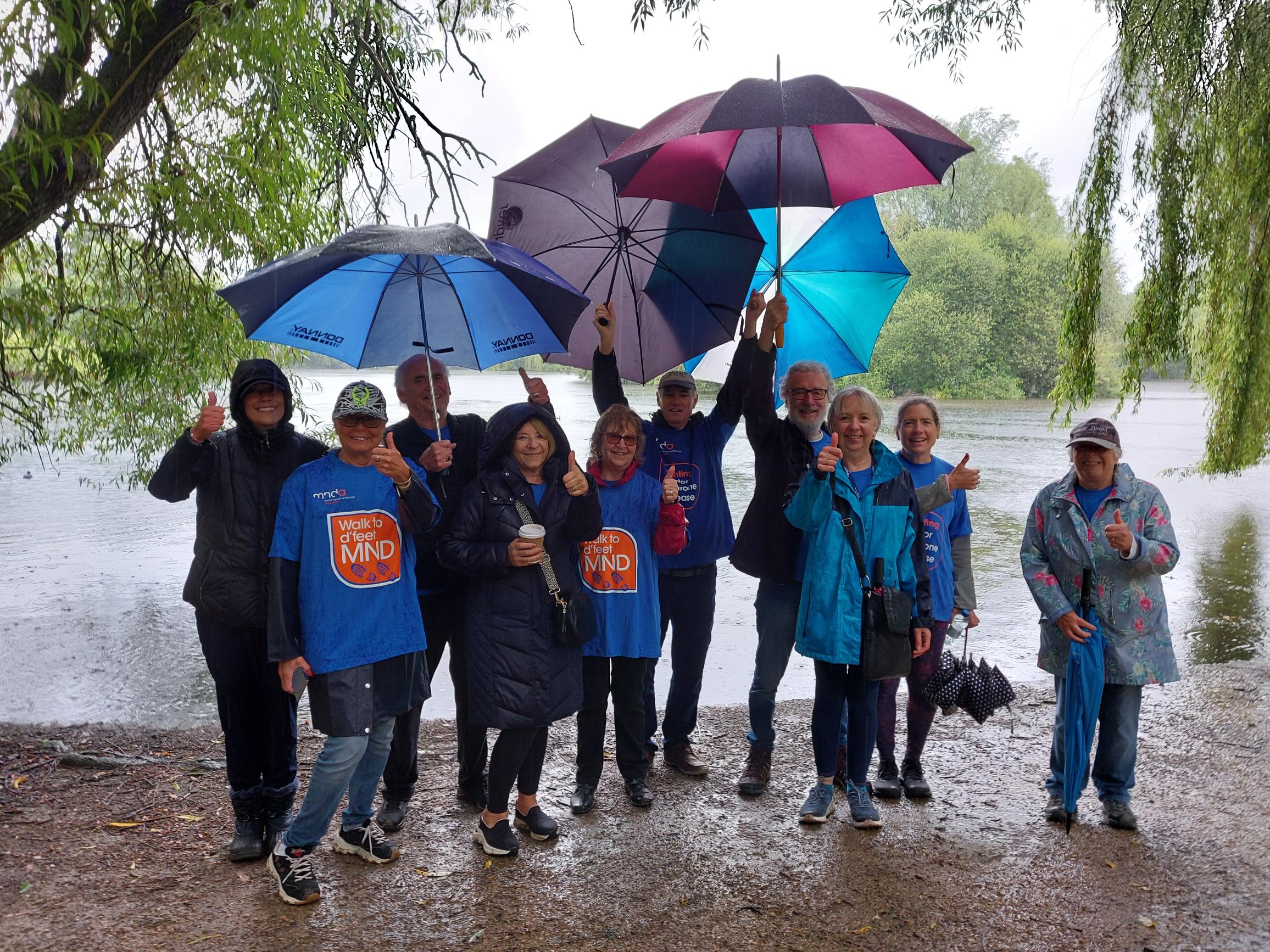 Volunteers and walkers at Stanborough Lakes holding umbrellas for the Hertfordshire branch's annual walk to d'feet. 