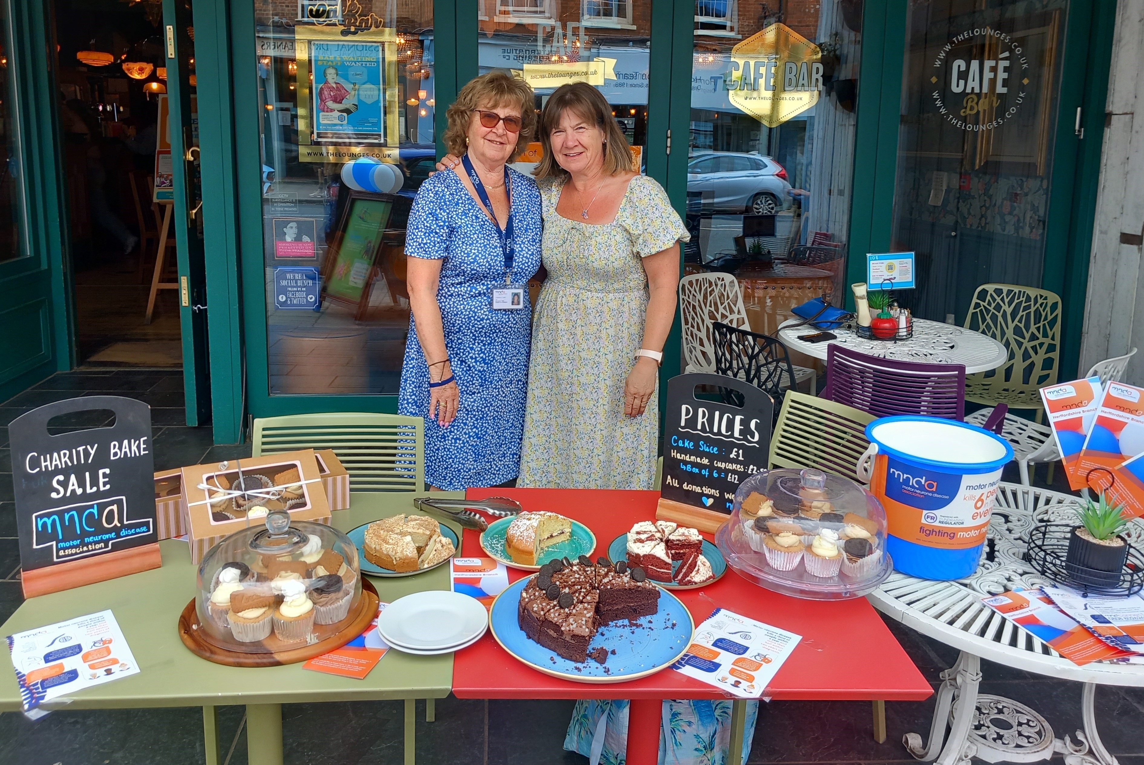 Christine and Helen stood outside Granello Lounge in front of a table of cakes. 
