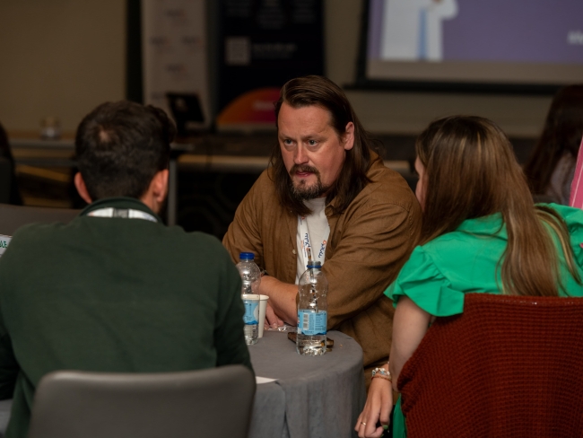 Martyn and Anna sitting at a table at the EnCouRage event, chatting with others